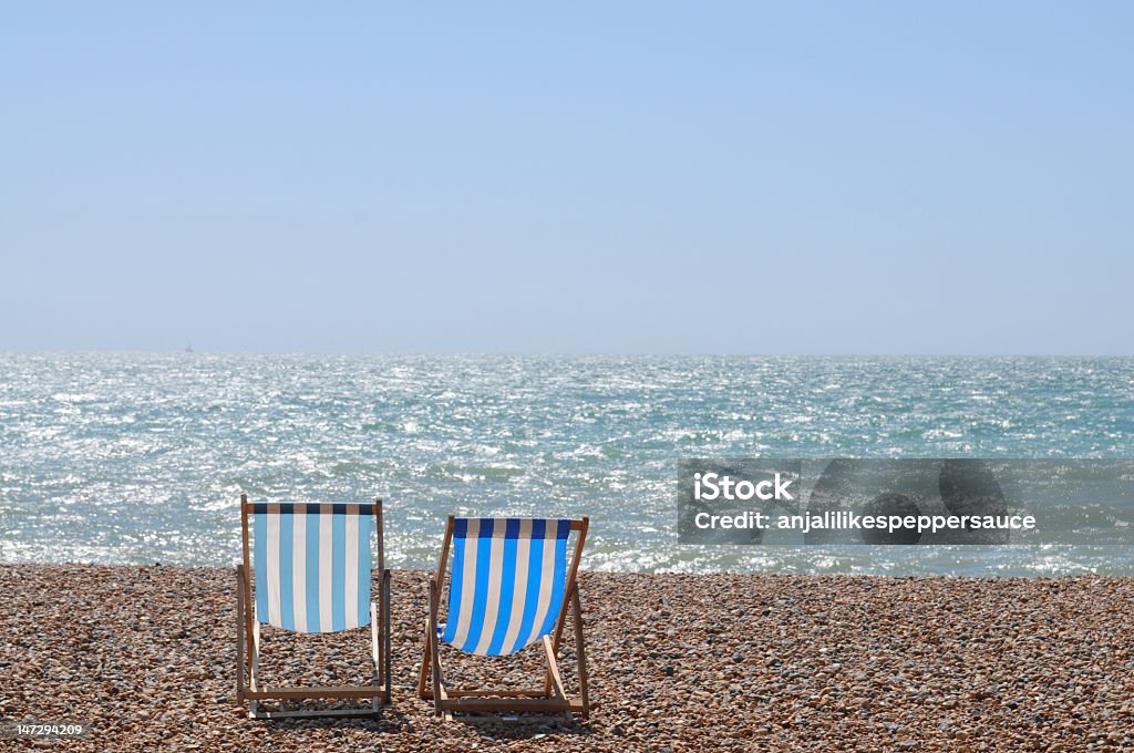 Two blue and yellow deckchairs on a shingle beach by the sea summer concept. chairs on brighton beach, england. Armchair Stock Photo