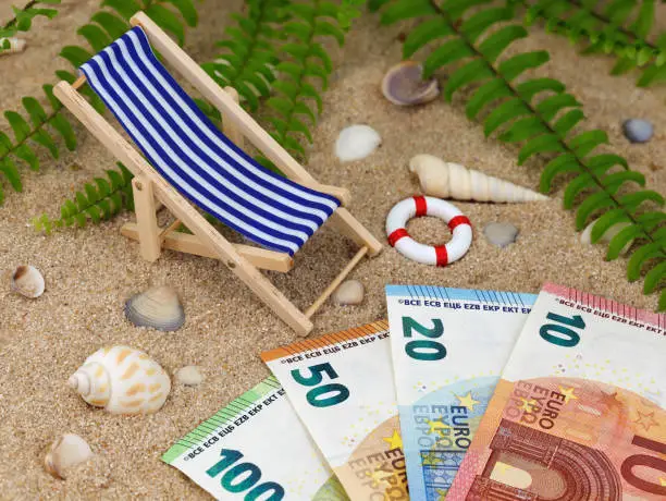 deck chair with euro banknotes in the sand with sea shells and tropical background, concept of saving money for a holiday trip or high vacation expenses.