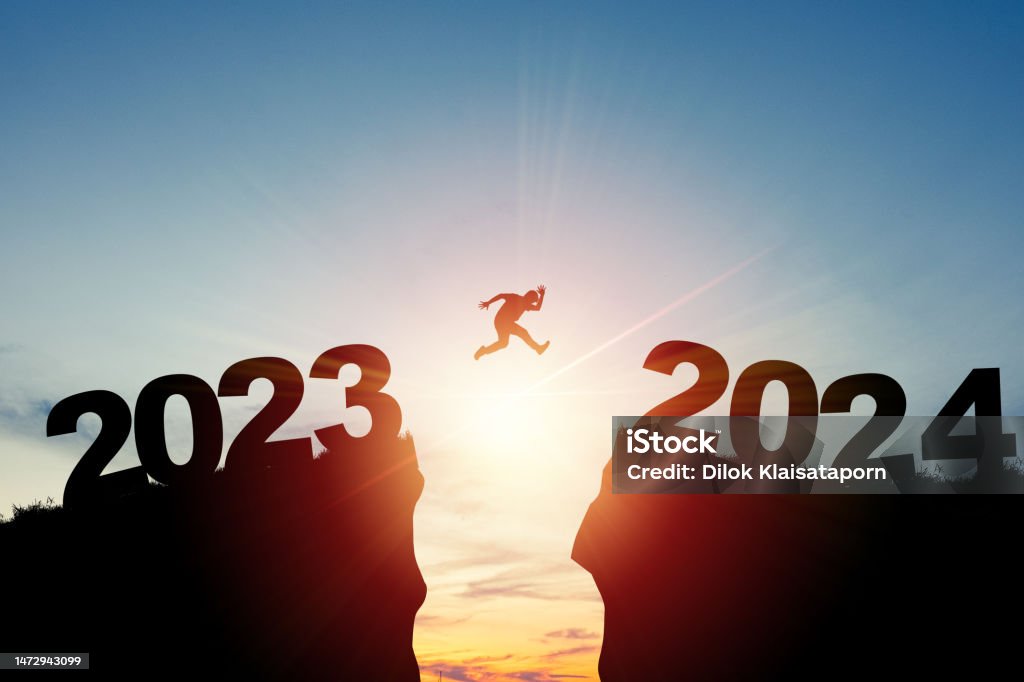 Welcome merry Christmas and happy new year in 2024,Silhouette Man jumping from 2023cliff to 2024 cliff with cloud sky and sunlight. 2024 Stock Photo