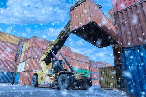 Crane lifting up container in yard on snow.