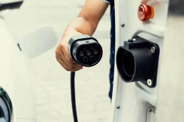Progressive concept of hand attaches an emission-free power connector to the battery of electric vehicle at home. Electric vehicle charging via cable from charging station to EV car battery