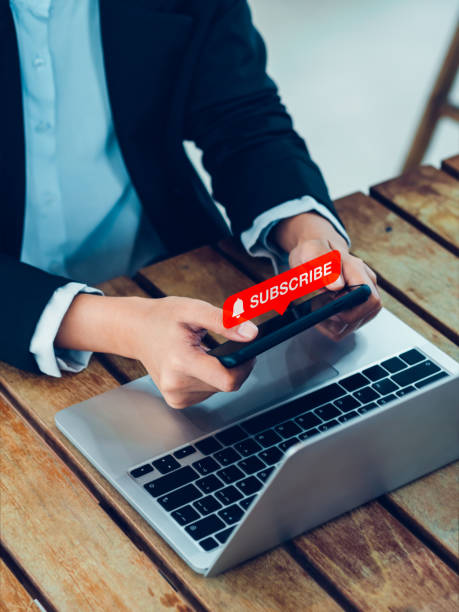 istock Subscription concept. Red subscribe button with bell icon appear on smart mobile phone in hands. Smartphone horizontal style holding by businesswoman who watching on entertainment applicatiion. 1472958207