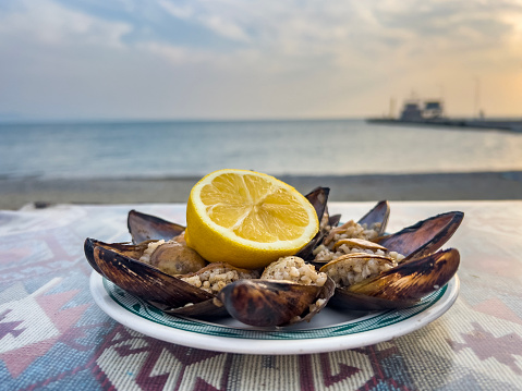 Turkish style stuffed mussels, called MIDYE DOLMA, served with a half cut fresh yellow lemon in an old fashioned style restaurant at the beach. Side view on mussels filled with rice and spices. Food background with copy space.