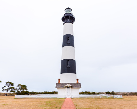 Bodie Island Lighthouse with light keeper's house, surrounded by white fence, Outer Banks, Nags Head, North Carolina, Cape Hatteras with red brick sidewalk leading up to small entry house and lighthouse.