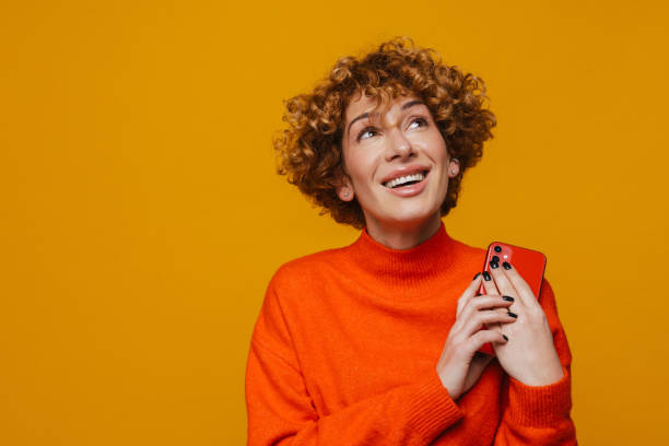 istock Pensive middle-aged woman holding smartphone while standing isolated 1472963842