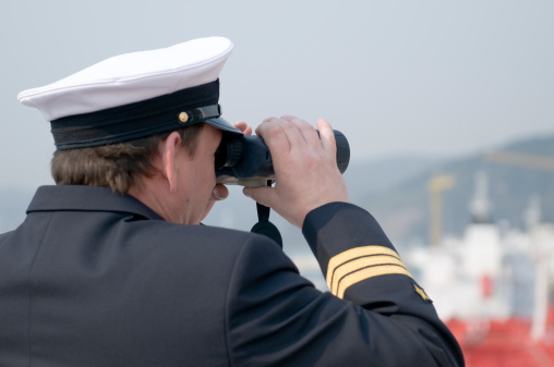 Navigation officer with binocular, looking ahead on the navigation bridge of ocean ship
