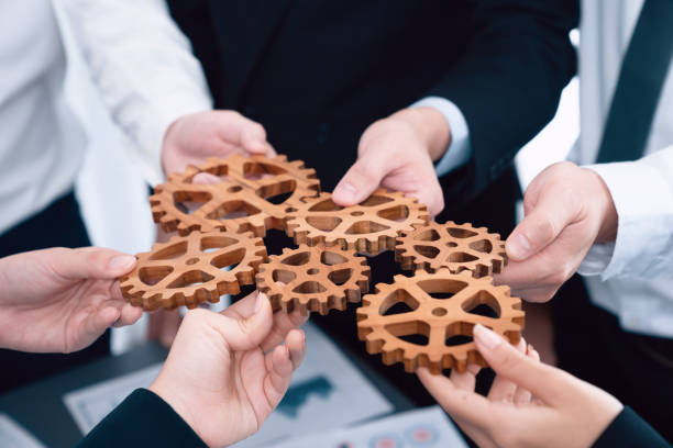istock Closeup top view hands holding gears over table with BI reports for harmony. 1472969720