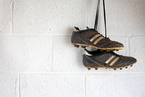 Pair of muddy black football boots A pair of muddy black football boots hang up in a white-walled changing room. There is room for copyspace. cleat stock pictures, royalty-free photos & images