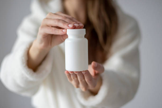 istock Woman is holding a white jar for tablets, pills, and supplements. Mock Up. 1472971191