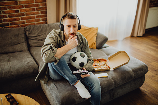 High-angle view of a young Caucasian man playing a football video game with a joystick at home.