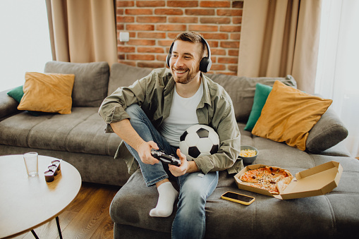 High-angle view of a happy young Caucasian man playing a video game with a joystick at home.