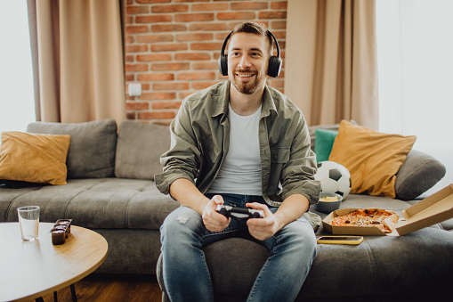 Happy young Caucasian man playing a video game with a joystick at home.