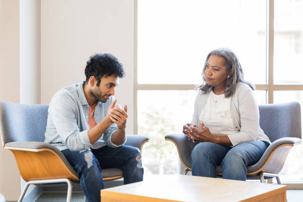 Young adult male gestures while speaking with his mental health therapist The young adult male gestures while speaking to his mental health therapist about a triggered experience he had yesterday at work. alternative therapy stock pictures, royalty-free photos & images