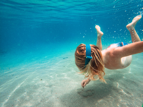 Underwater exploration. Small blond hair boy using blue swimming googles while drawing a shape into the sand.