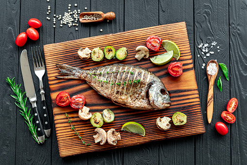 Grilled Dorada fish, sea bream with the addition of spices, herbs and lemon on the grill plate. Fried fish with vegetables
