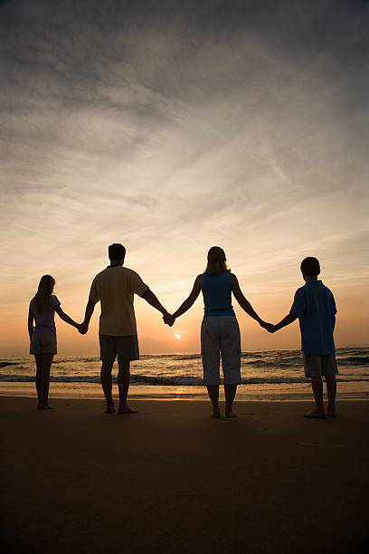A family holding hands on a beach during sunset stock photo