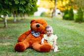 a smiling baby is sitting on the green grass with a large Teddy bear in a yellow summer dress in summer, #summer background