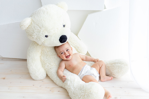 A small child a girl 6 months old is lying on a large soft bear in a bright apartment in diapers
