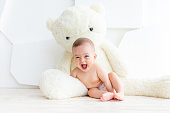 A small child a girl of 6 months is sitting with a large soft bear in a bright apartment in diapers