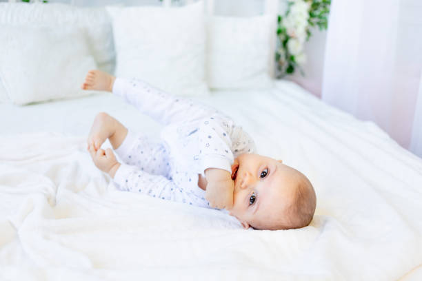 a smiling little boy lying on a white bed, hands in his mouth. space for text. Teething A smiling little boy lying on a white bed, hands in his mouth. space for text. Teething half dozen babies stock pictures, royalty-free photos & images