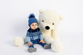 a smiling little boy is sitting in Winter clothes with a large Teddy bear