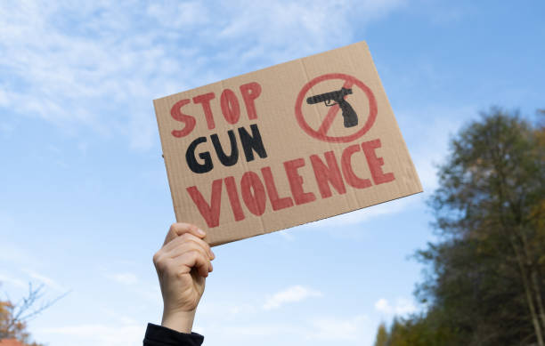 Stop Gun Violence placard sign at protest rally demonstration strike to ban weapons and end shooting. Hand holding a sign with slogan Stop Gun Violence and black pistol strikethrough. Woman with placard at protest rally demonstration strike to ban weapons and end shooting. end gun violence stock pictures, royalty-free photos & images