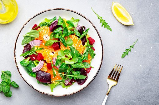 Beet and orange healthy salad with arugula, lamb lettuce, red onion, walnut and tangerine, gray kitchen table. Fresh useful vegan dish for healthy eating