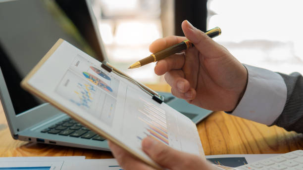 Business finance manager holding financial graph document to analyze company monthly expenses while sitting in the office Holding chart and graph paper in hand with laptop on table gerente de finanzas empresariales sosteniendo un documento gráfico financiero para analizar los gastos mensuales de la empresa mientras está sentado en la oficina sosteniendo un cuadro y papel cuadriculado en la mano con una computadora portátil sobre l