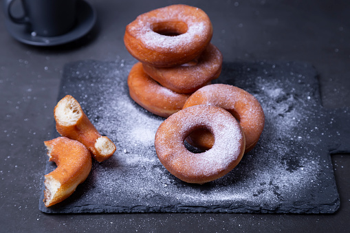 Пончики с сахарной пудрой. Традиционные пончики в форме кольца, жареные в масле (во фритюре), на чёрном фоне. Вредная еда. Крупный план