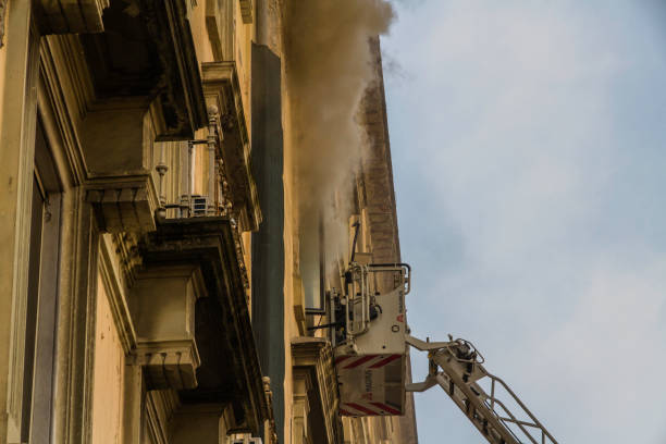 Editorial, Domestic apartment fire with smoke billowing from window. Garibaldi Square, Naples, Italy. Magirus Fire engine ladder extended with basket or cage, people at Garibaldi Station. - fotografia de stock