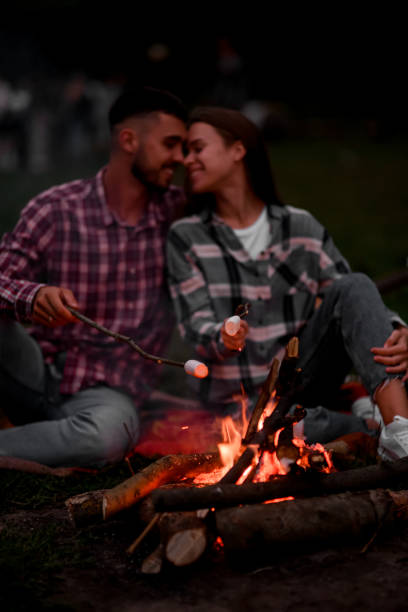 istock Happy smiling couple roasting marshmallows on campfire on nature. 1472986895