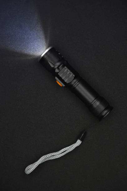 istock Metal black flashlight on a black background. Burning pocket flashlight close-up. Lighting device. 1472989010