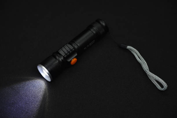 istock Metal black flashlight on a black background. Burning pocket flashlight close-up. Lighting device. 1472989043