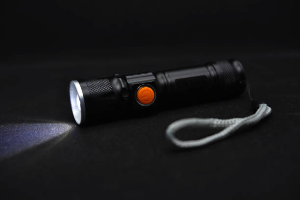 istock Metal black flashlight on a black background. Burning pocket flashlight close-up. Lighting device. 1472989085