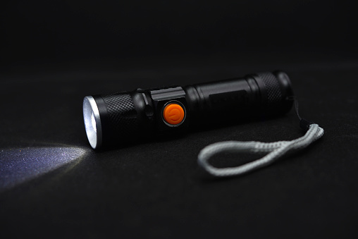 Metal black flashlight on a black background. Burning pocket flashlight close-up. Lighting device.