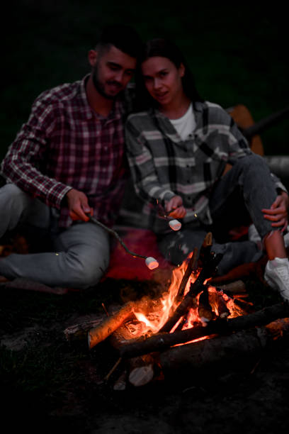 istock Happy couple roasting marshmallows on campfire on nature. 1472989100