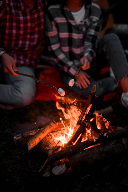 istock selective focus on marshmallows on stick over fire held by man and woman. 1472990033