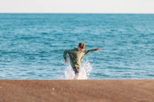 istock Boy running in waves at the beach in wet clothes 1472993946