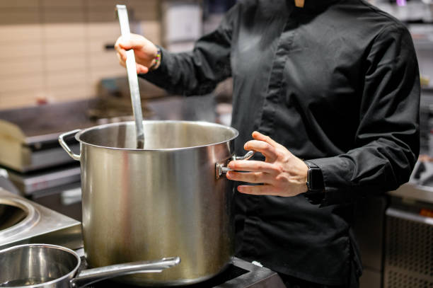 chef pouring tasty soup from big pot into bowl on restaurant kitchen