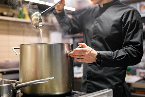 chef pouring tasty soup from big pot into bowl on restaurant kitchen