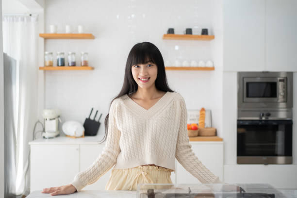 istock Young beautiful modern Asian woman stands near table on kitchen at home. 1472995444