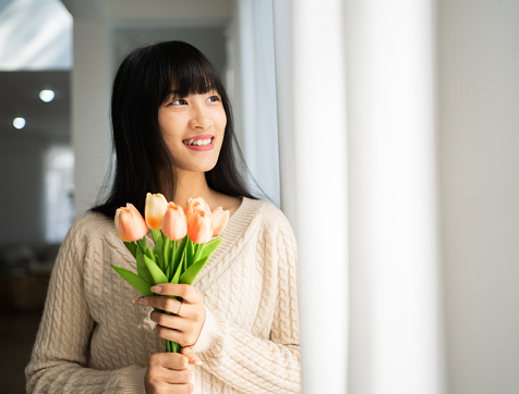 Beautiful Asian girl in the white sweater  with flowers and tulips in her hands on a home.