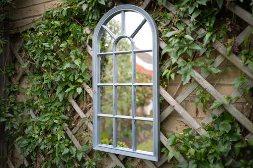 Shallow focus of a secret garden showing a ornate mirror seen attached to a trellis with vines growing around the frame.
