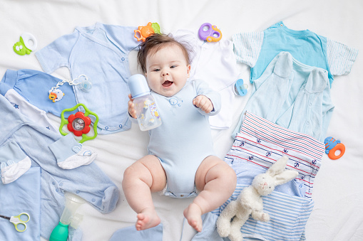 a baby in blue clothes is lying among children's accessories and clothes