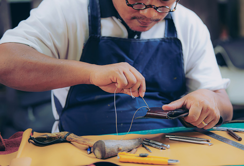 An experienced tanner sews a clasp for a leather product with stitches.