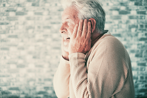 Desperate frustrated senior man in pain with hands on ears, elderly man alone at home suffering from divorce, bad relationship, mental illness needed support and care