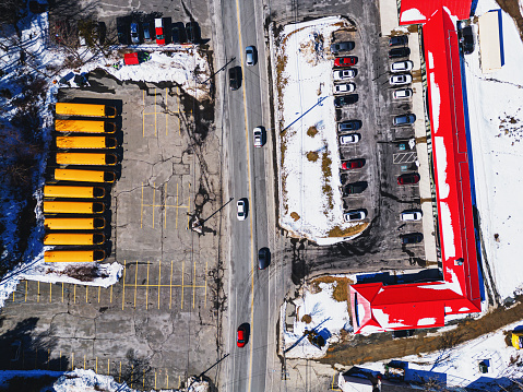 Aerial drone view of a fleet of school buses opposite a retail plaza.