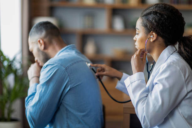 Black woman general practitioner checking sick man lungs with stethoscope stock photo