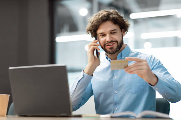 istock Smiling man using credit card talking on smartphone 1473016462