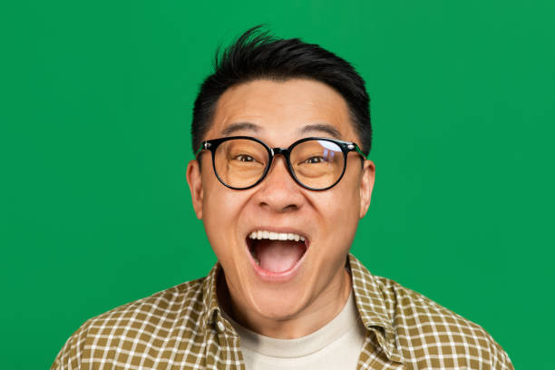 concetto di realizzazione. uomo asiatico maturo emotivo che applaude e urla, celebrando la vittoria su sfondo verde - la bocca apre foto e immagini stock